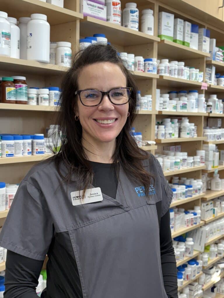 Pharmacy assistant smiling in front of medicine shelves.
